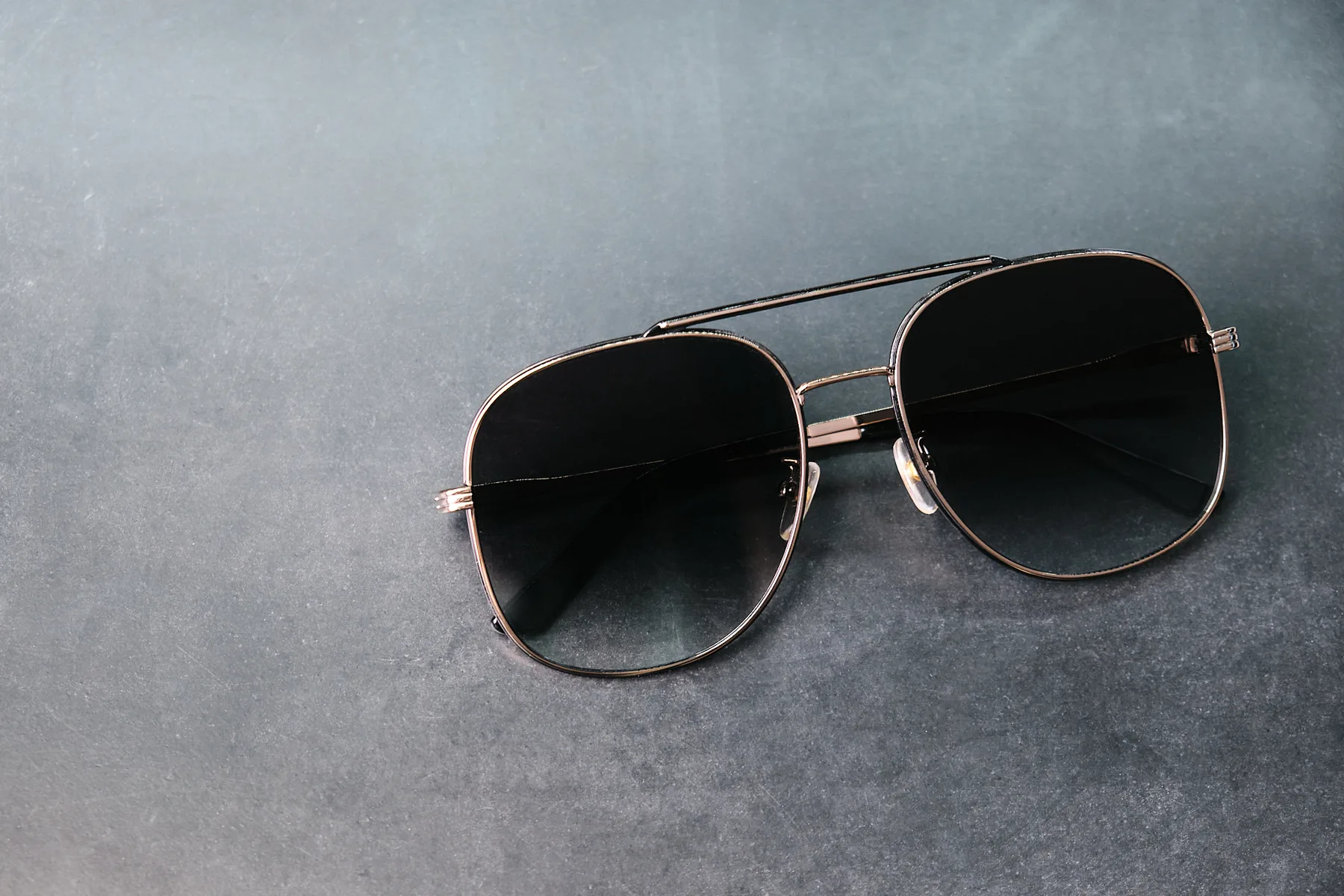 A gold Kolari Shades Aviator on dark slate
